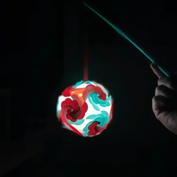 A beautifully crafted 3D printed orb with red and teal designs, suspended in an indoor setting, showcasing its potential as a unique decorative piece for B2B applications.