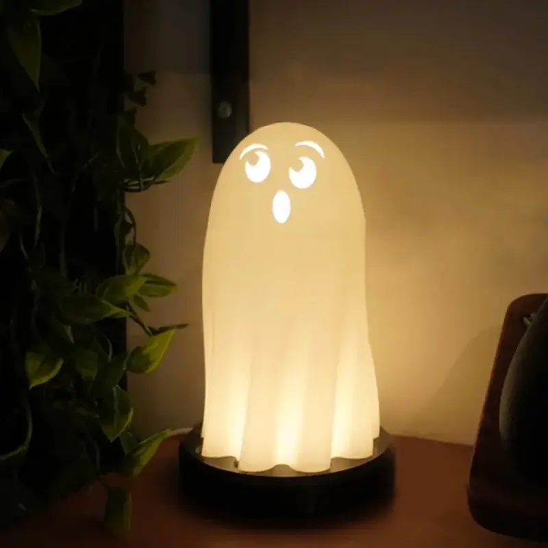 A 3D printed Halloween ghost lamp emitting a warm glow on a wooden table, surrounded by green plants