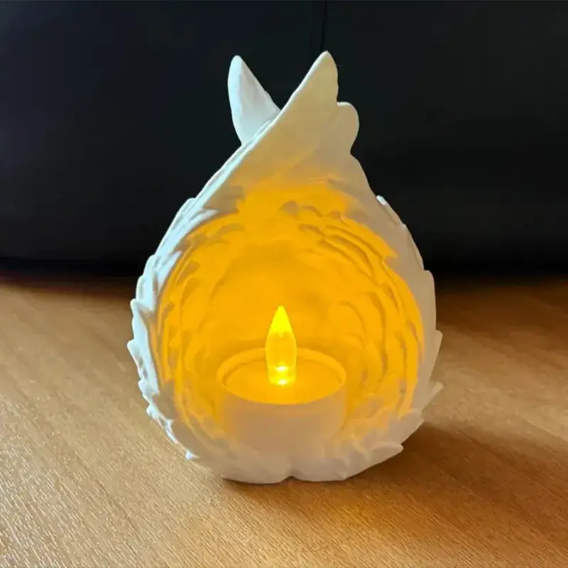 White 3D printed angel wing tea light emitting soft glow through intricate feather details