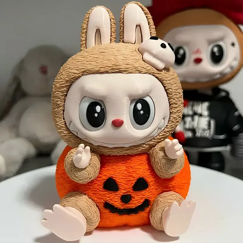 3D printed Pumpkin Labubu figure wearing brown bunny ears and orange costume with ghost pattern, holding skeletal accessory
