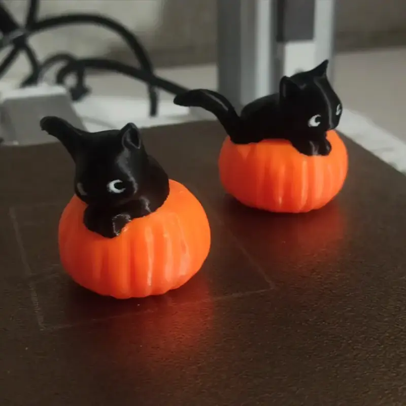 Two 3D printed Halloween cat and pumpkin ornaments on a dark surface, showcasing cute and festive designs for B2B clients