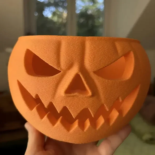 Close-up of an artisanal 3D printed pumpkin bowl with a menacing jack-o'-lantern face, ready to hold treats for commercial use