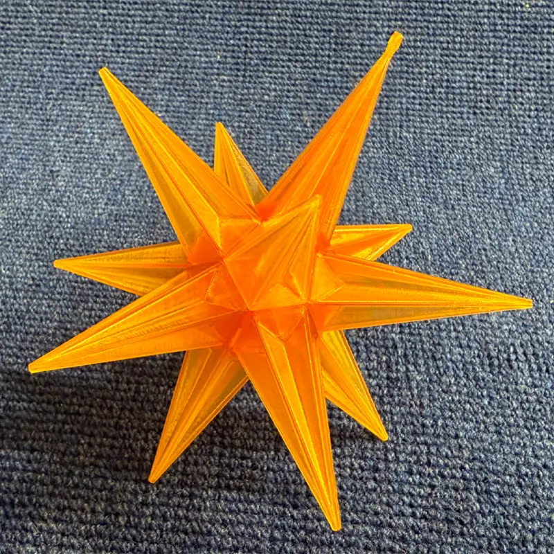 Bright orange 3D printed Christmas star tree topper with eight points on blue fabric background