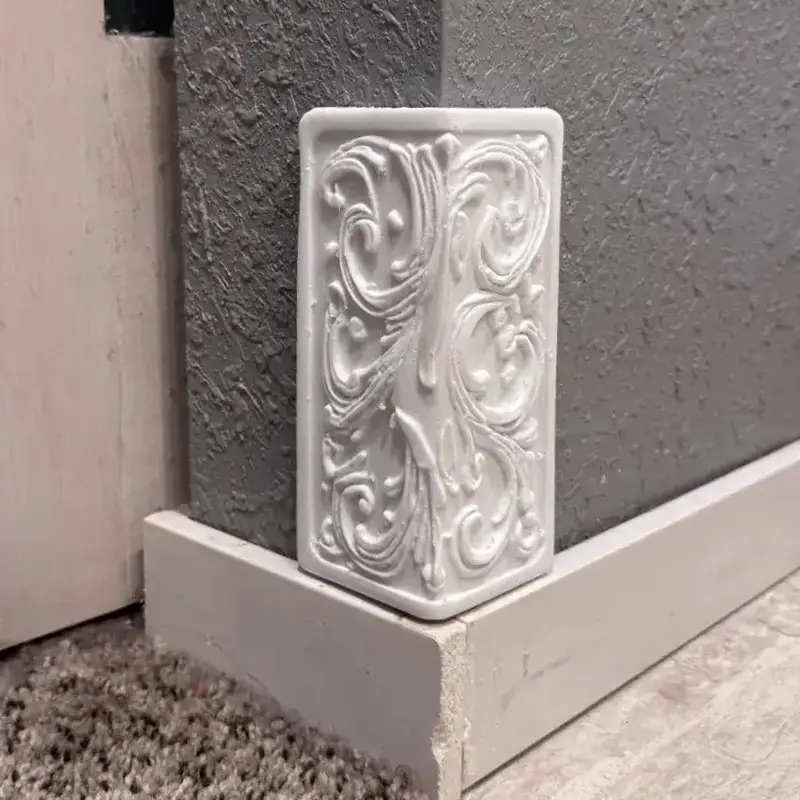 White 3D printed Baroque ornamental edge guard with intricate swirls and floral motifs installed on gray wall