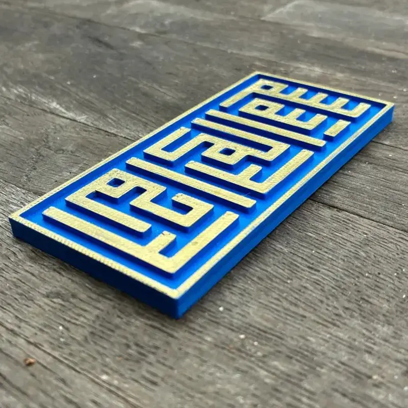 Blue and gold geometric Kufic art panel featuring LISBLEE script in square Kufic style, displayed on wooden surface