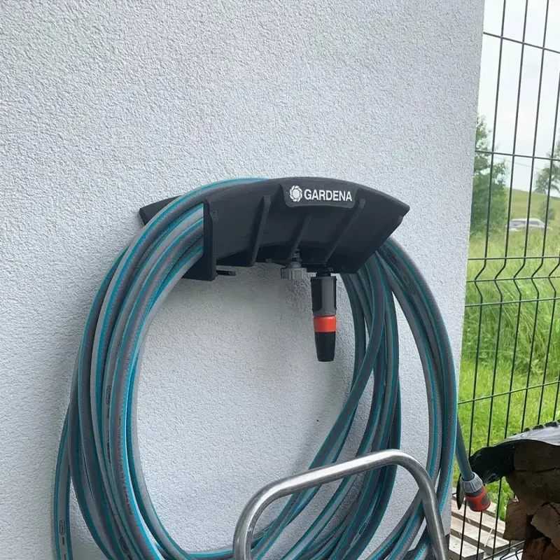 Black 3D printed hose management bracket mounted on white wall, holding a coiled GARDENA garden hose for organized storage