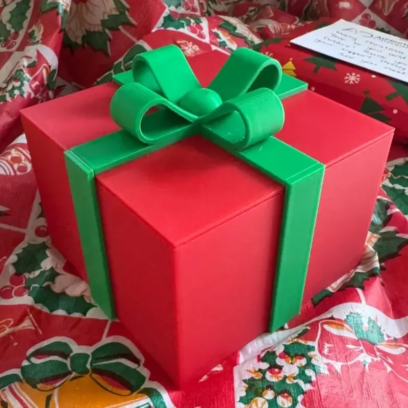 Red 3D printed Christmas gift box ornament with green bow on festive tablecloth