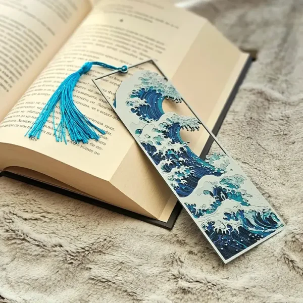 Blue 3D printed Kanagawa wave bookmark with detailed wave patterns and tassel, resting on an open book with a soft furry background