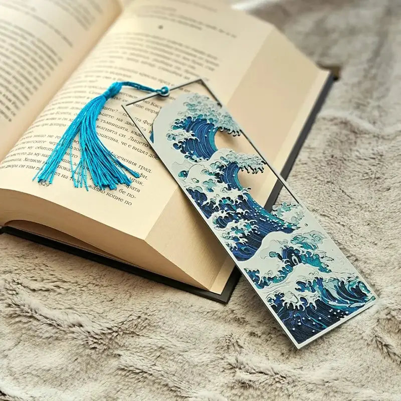 Blue 3D printed Kanagawa wave bookmark with detailed wave patterns and tassel, resting on an open book with a soft furry background