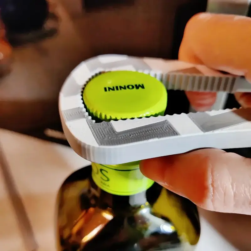 A hand using a custom bottle opener to open a bottle with a green cap, showcasing its ergonomic design