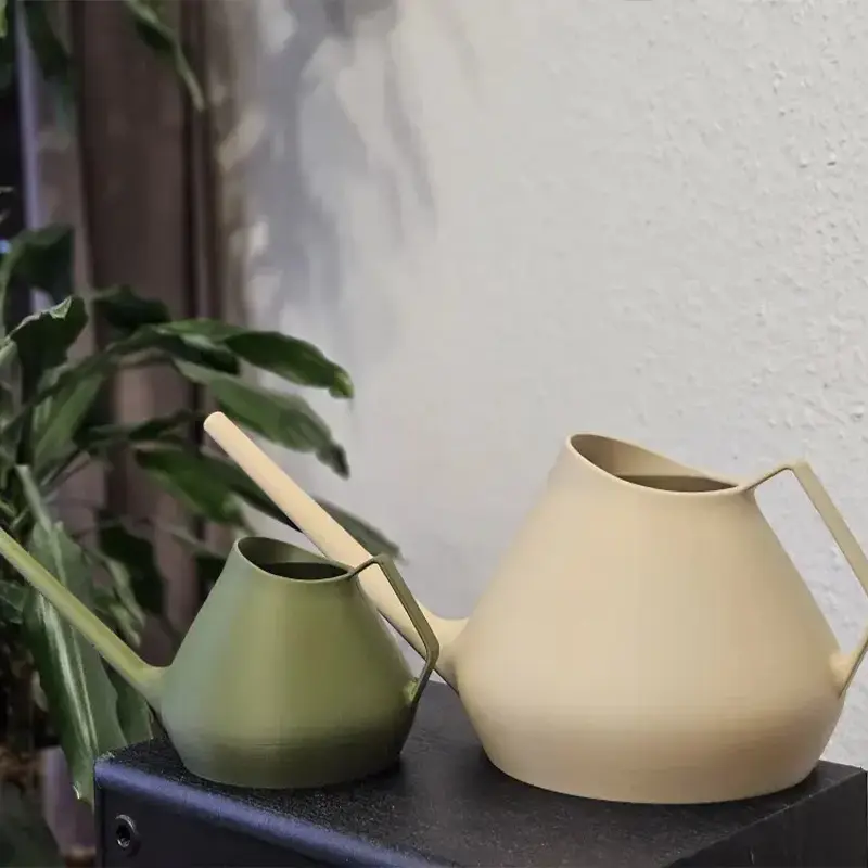 Premium 3D printed watering cans in olive green and sand white colors, showcasing sleek design on dark surface with plant background