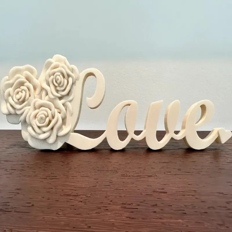 White 3D printed wedding LOVE sculpture with cursive letters and rose designs on dark background