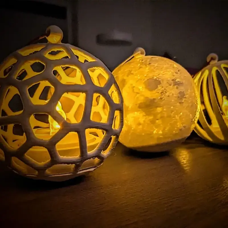 Set of three custom 3D printed Christmas ball lights with LED illumination, showing lattice and moon patterns, glowing on a wooden table