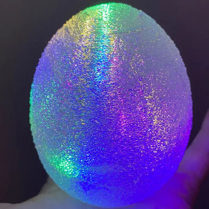 Close-up of iridescent 3D printed light sphere showing blue-purple-green color shift and spiral texture on dark background