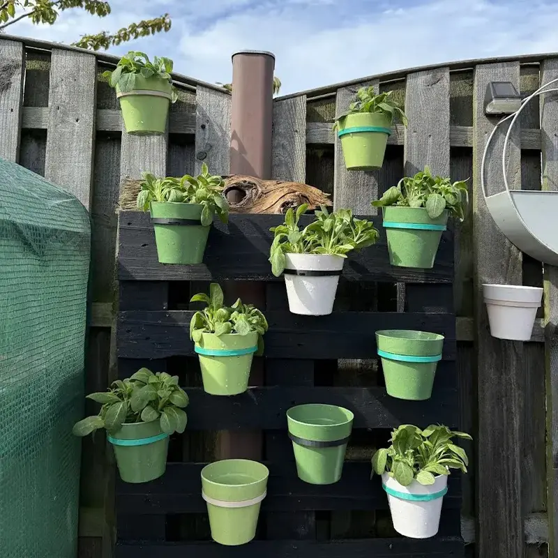 Simple pot mounting clip holding green plant on wooden fence, demonstrating easy vertical gardening solution