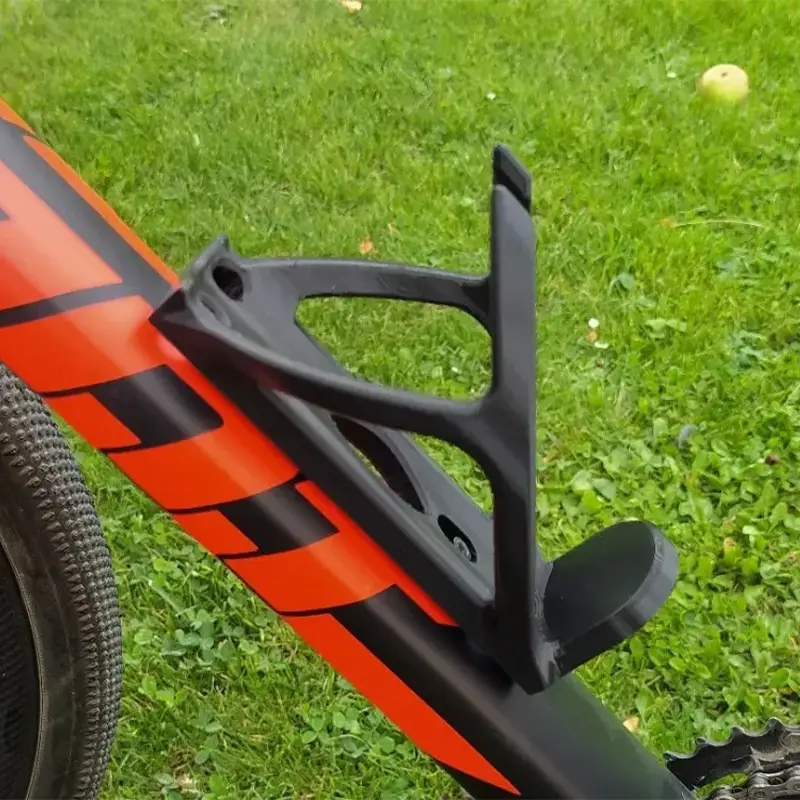 Black 3D printed performance hydration mount installed on orange bicycle frame against natural background