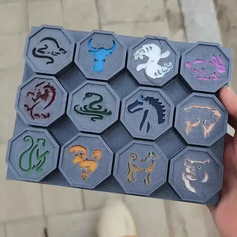 A hand holding a board with twelve hexagonal 3D-printed zodiac medallions, each featuring a different animal design for B2B clients