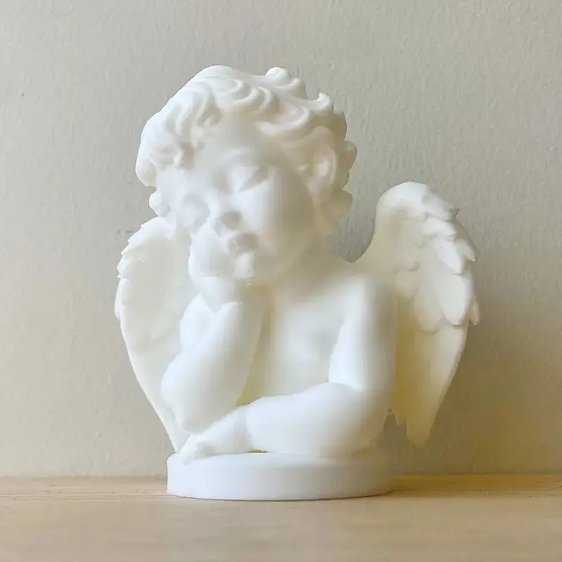 White 3D printed slumbering cherub ornament with detailed wings resting on light wooden surface